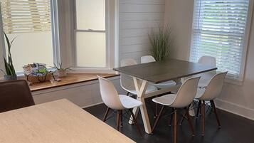 Un coin repas avec une table et des chaises, une plante en pot et une fenêtre avec des stores.