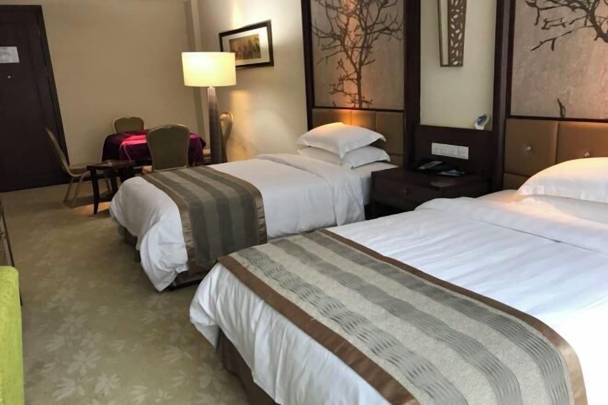 Habitación de hotel con dos camas, un escritorio, una silla, una lámpara y obras de arte en las paredes.