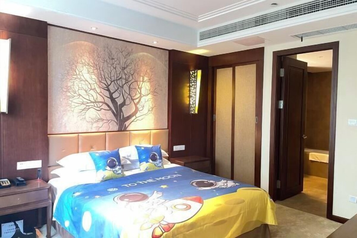 Habitación de hotel con cama, mesita de noche, un cuadro de un árbol y una puerta que da a otra habitación.