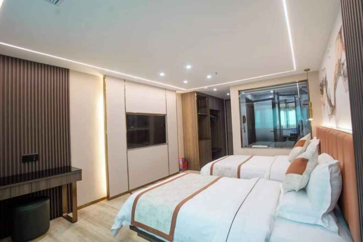 A modern hotel room with two beds, a desk, a wardrobe, and a large window.