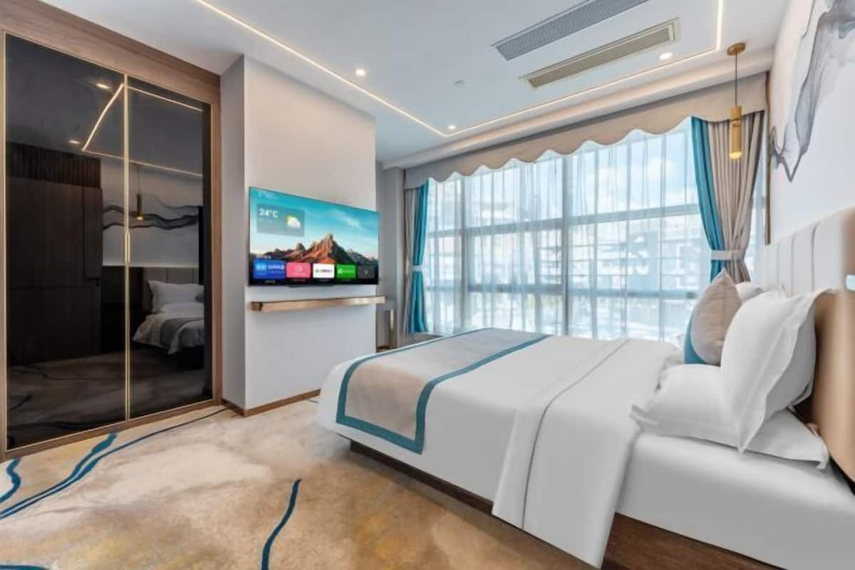 A hotel room with a bed, a TV, a wardrobe, and a large window with curtains.