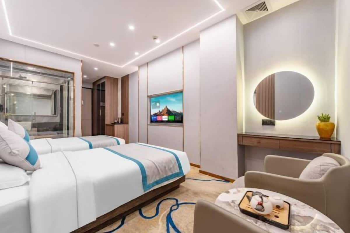 A modern hotel room with a bed, a seating area, a TV, and a mirror.