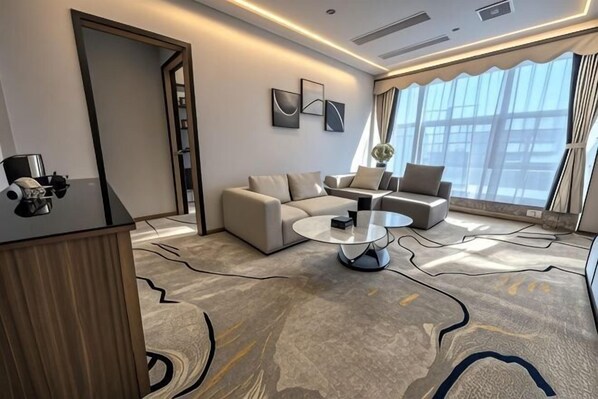A modern hotel room with a sofa set, a coffee table, a desk with a computer, and large windows. - Xiangxing Hotel (Zhongshan)