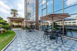 An outdoor patio with tables and umbrellas, a pergola, and a view of a modern building.