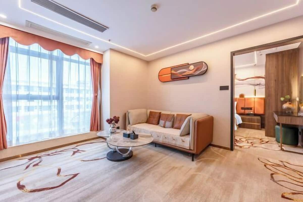 A modern hotel room with a sofa, coffee table, and a large window with curtains.