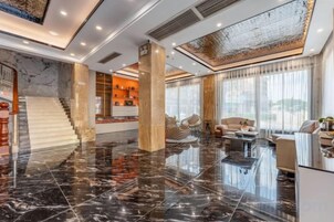 A spacious lobby with a marble floor, a staircase, and a reception area.
