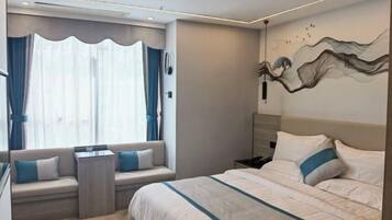 A modern hotel room with a large bed, a seating area with a view, and a decorative wall piece.