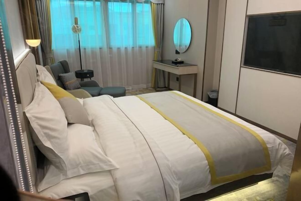 A hotel room with a bed, a desk, a chair, a mirror, and a window.
