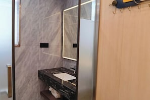 A modern bathroom with a marble wall, a glass shower enclosure, and a wooden door. - Xiangxing Hotel (Zhongshan)