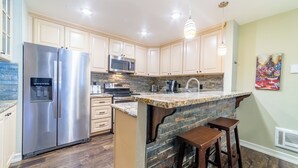 A modern kitchen with stainless steel appliances, a granite countertop island, and wooden bar stools. - Beautiful St Moritz Family Home 560 (Mammoth Lakes)