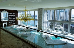 A spacious indoor area with a large window overlooking a cityscape, a marble floor, and a pool area with seating.