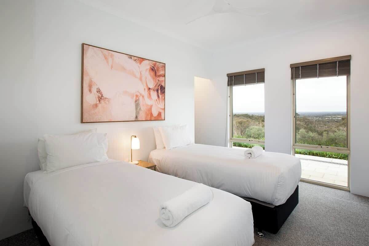 Une chambre d’hôtel avec deux lits, une grande peinture abstraite et une vue sur le paysage par les fenêtres.