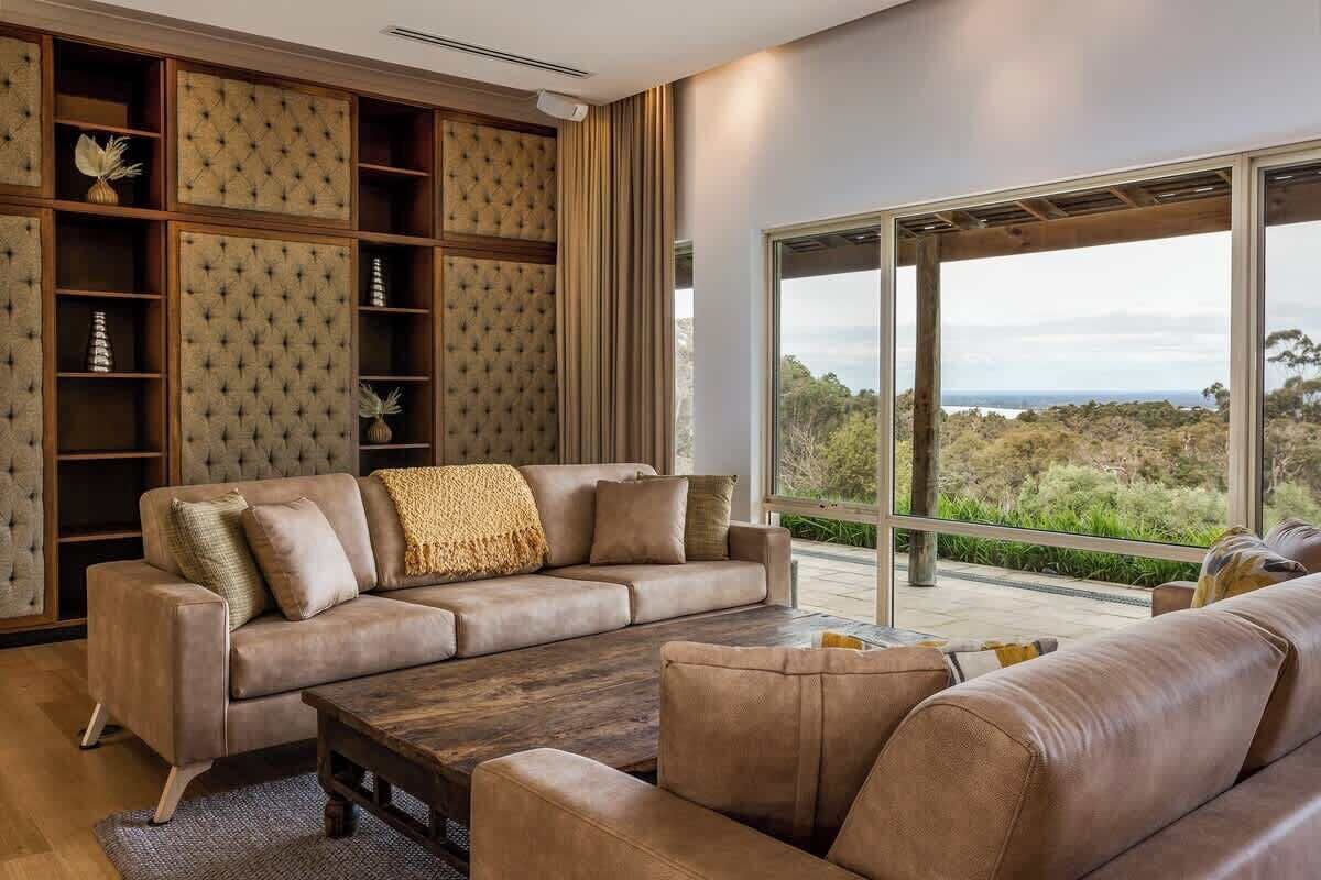 A modern living room with a leather sofa, a wooden coffee table, and a large window offering a view of the outdoors.