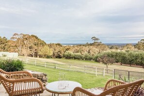 Un espace extérieur aménagé avec des chaises en osier et une table en verre, offrant une vue sur un paysage verdoyant, avec des arbres et un panorama lointain.