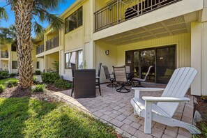 A building with a covered patio area, outdoor seating, and a palm tree.