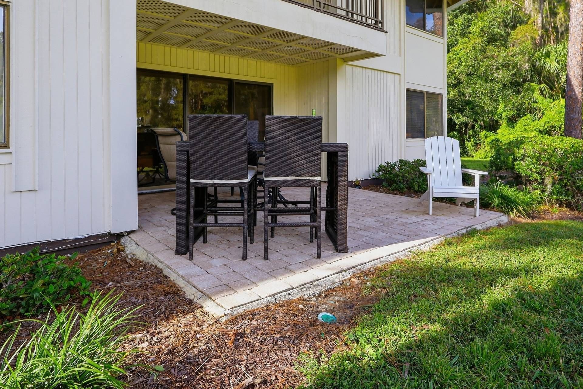 A patio with two wicker chairs and a white Adirondack chair outside a building with a yellow awning.