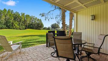 Une terrasse avec mobilier d’extérieur, une vue sur un terrain de golf et un bâtiment dont le revêtement extérieur est constitué de panneaux verticaux.