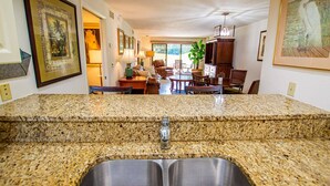 A kitchen with granite countertops, stainless steel sink, and a dining area with wooden furniture. - 2BR Ground Floor Golf Retreat | King Suite | Saddlebrook | Optional Amenities | Golf Course Views (Wesley Chapel)