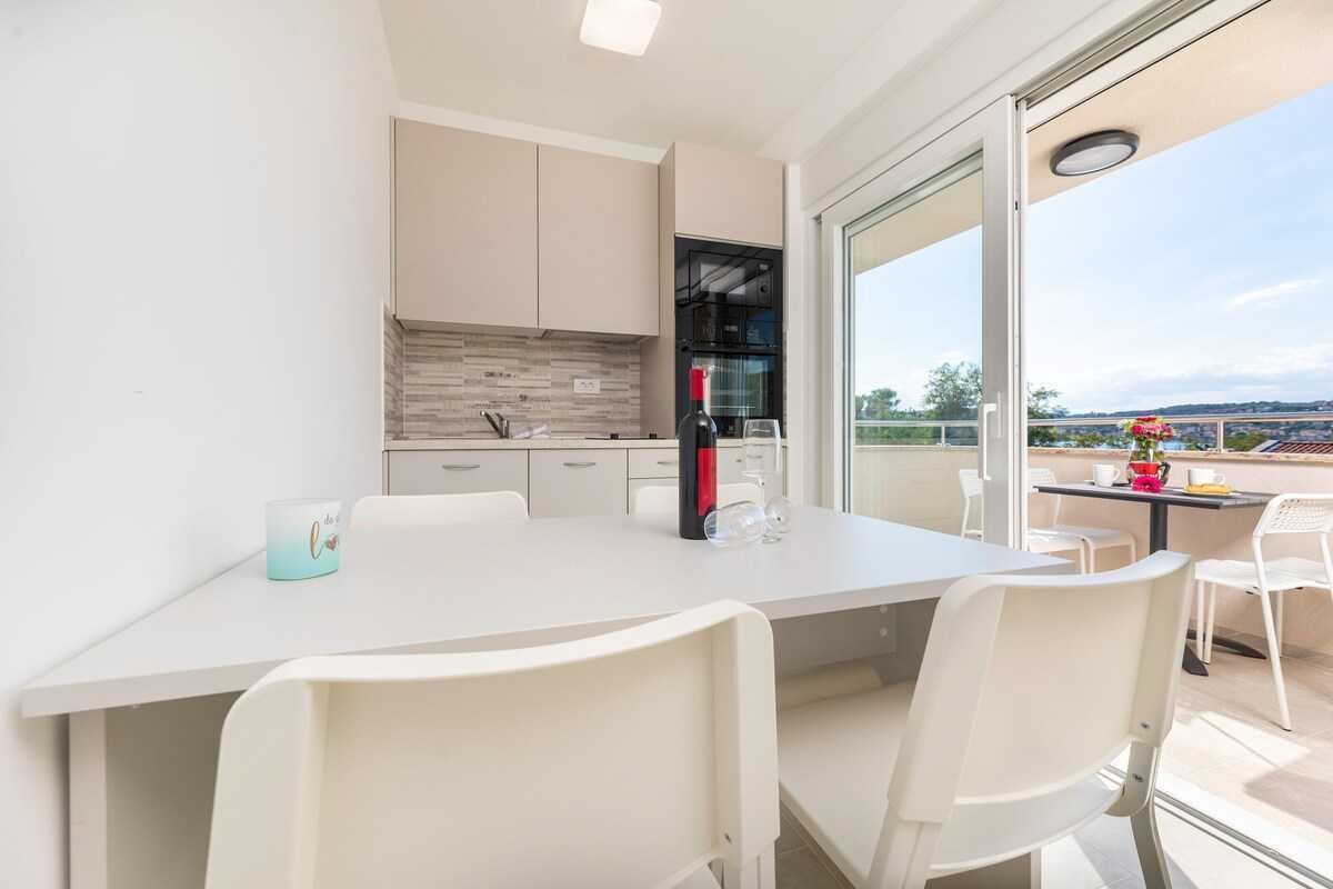A modern kitchen with white cabinets, a white countertop, and a dining area with white chairs.