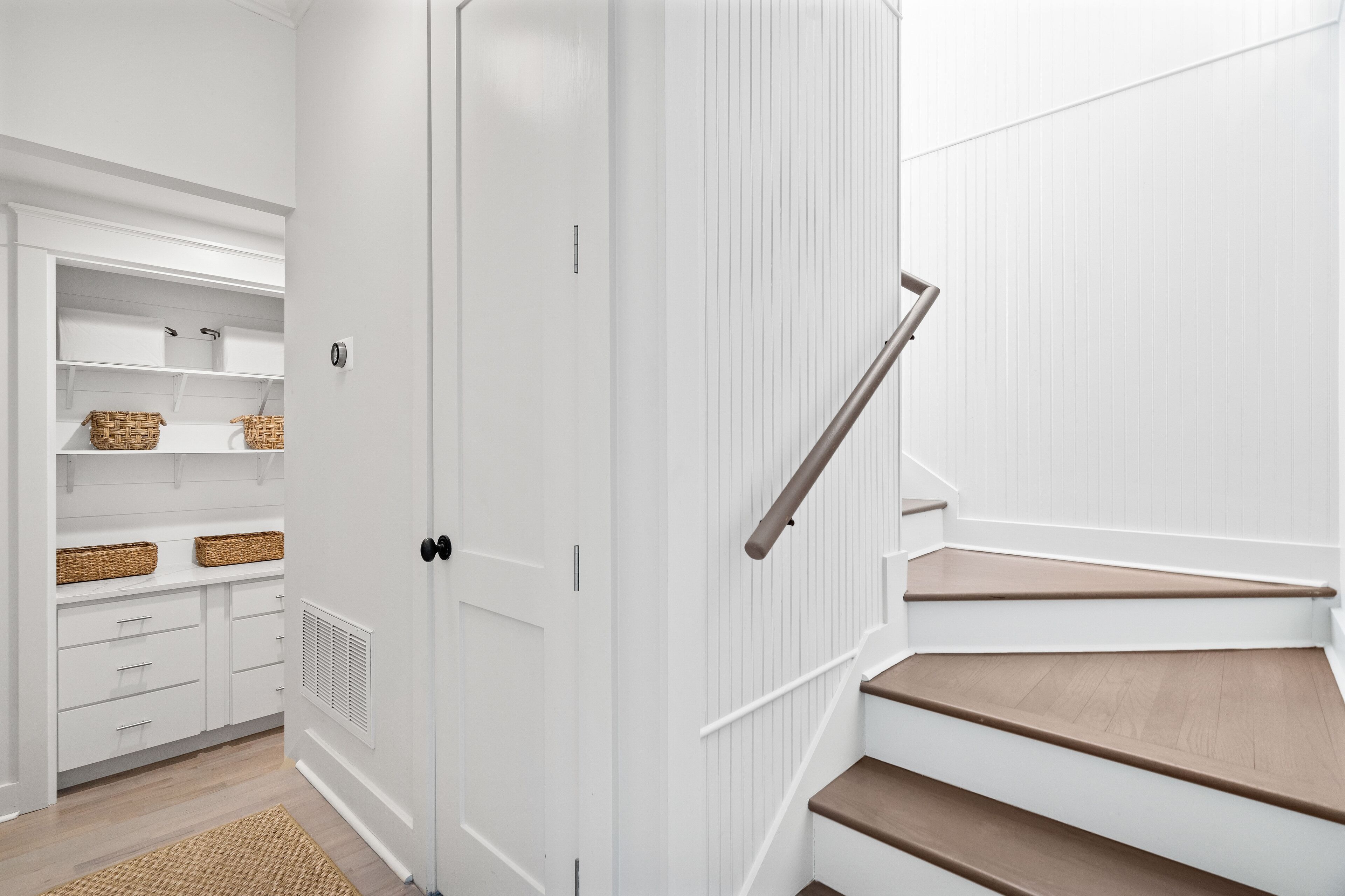 Un interior limpio y luminoso, con una escalera de madera, estanterías empotradas y cestos de mimbre.