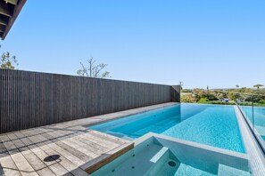 A modern outdoor swimming pool with a wooden deck and a metal railing.