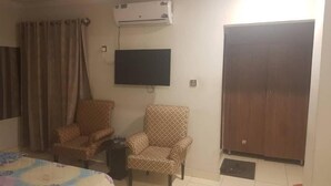 A room with two patterned armchairs, a flat-screen TV, an air conditioner, and a wardrobe.