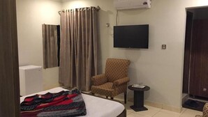 A hotel room with a bed, a chair, a small table, a TV, and a shower curtain.