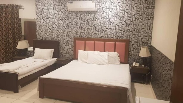 A hotel room with two single beds, a large bed, a patterned wall, an air conditioner, and a nightstand with a lamp.