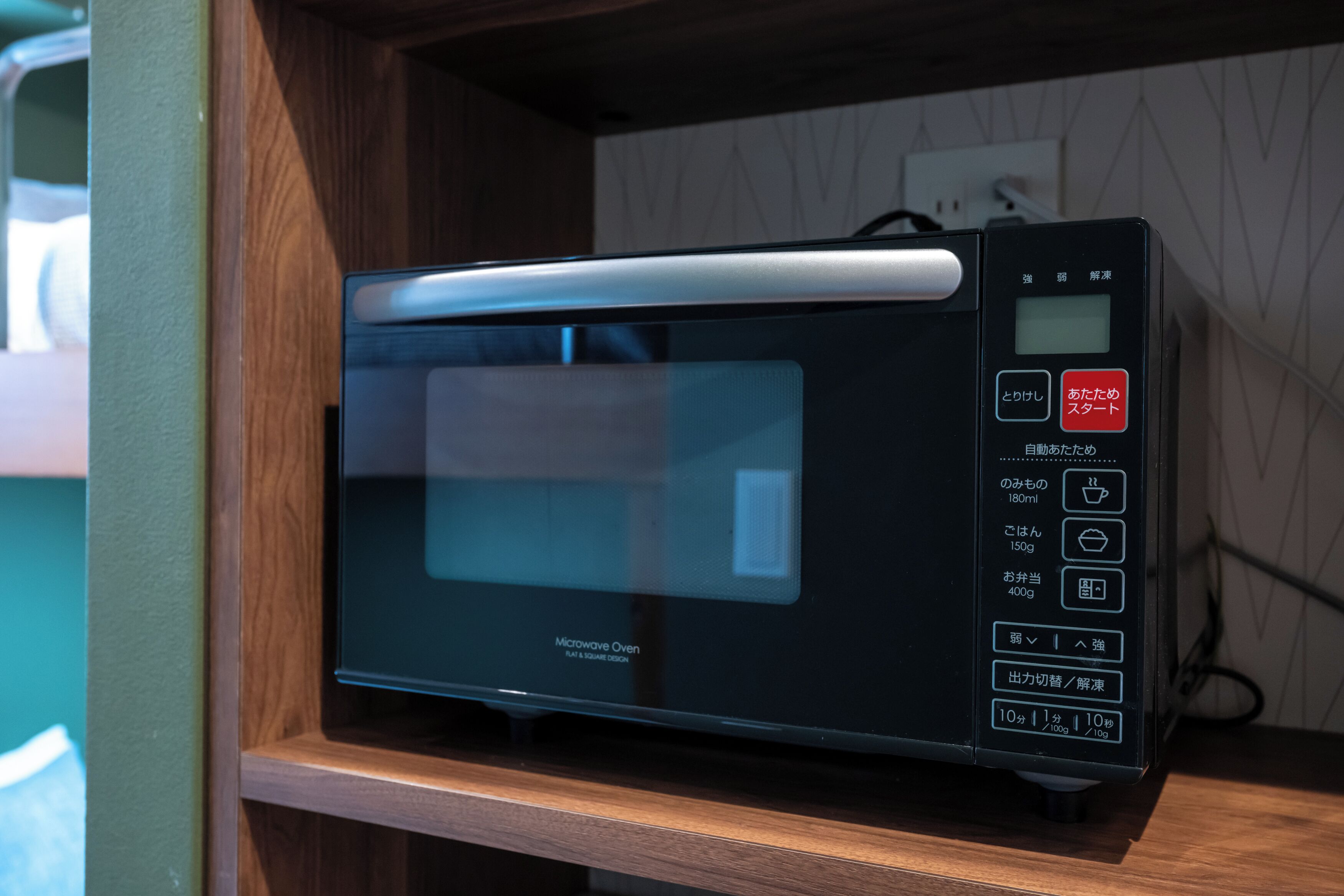 A microwave oven with a digital display and control panel, placed on a wooden shelf.