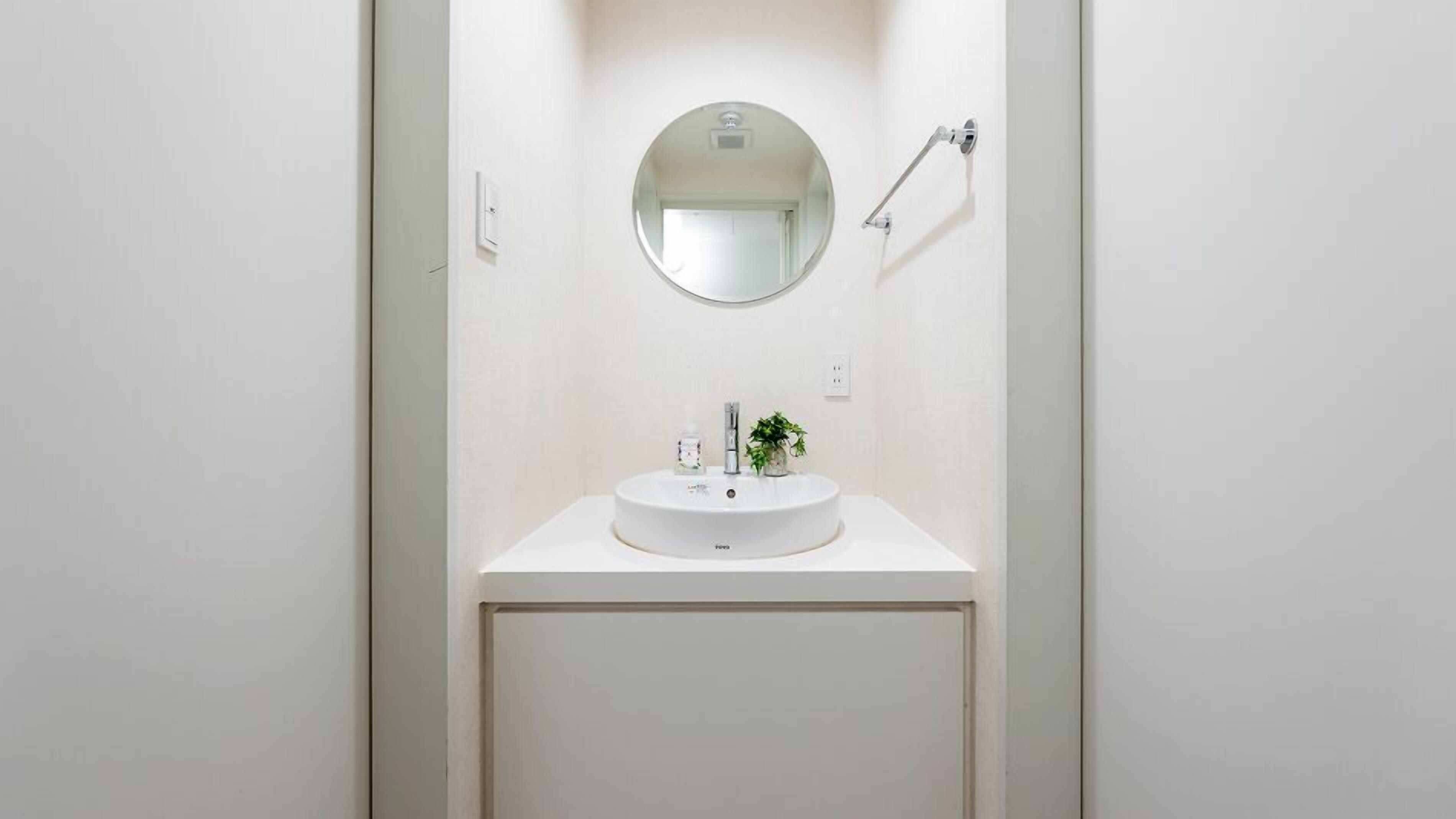 A bathroom with a round mirror, a sink, and a shower head.