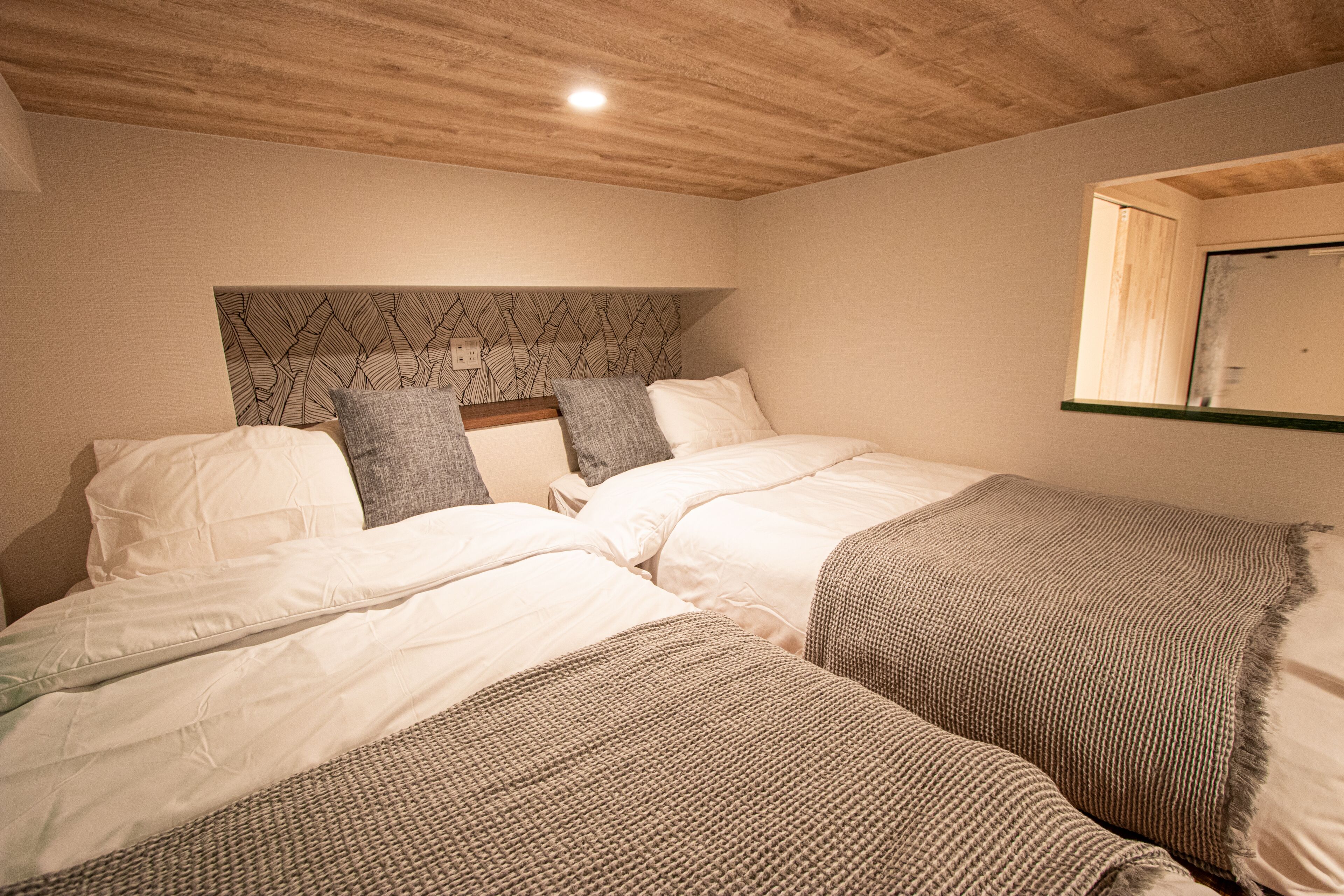 A bedroom with two beds, a wooden ceiling, and a headboard with a leaf pattern.