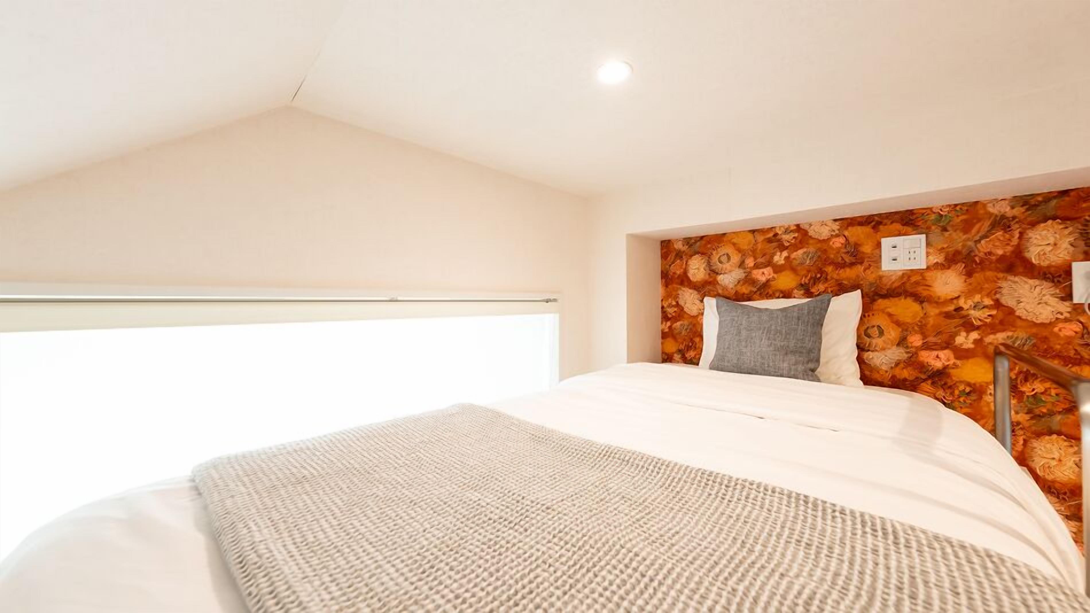 A bedroom with a sloped ceiling, a large window, a bed with white bedding, and a floral-patterned headboard.