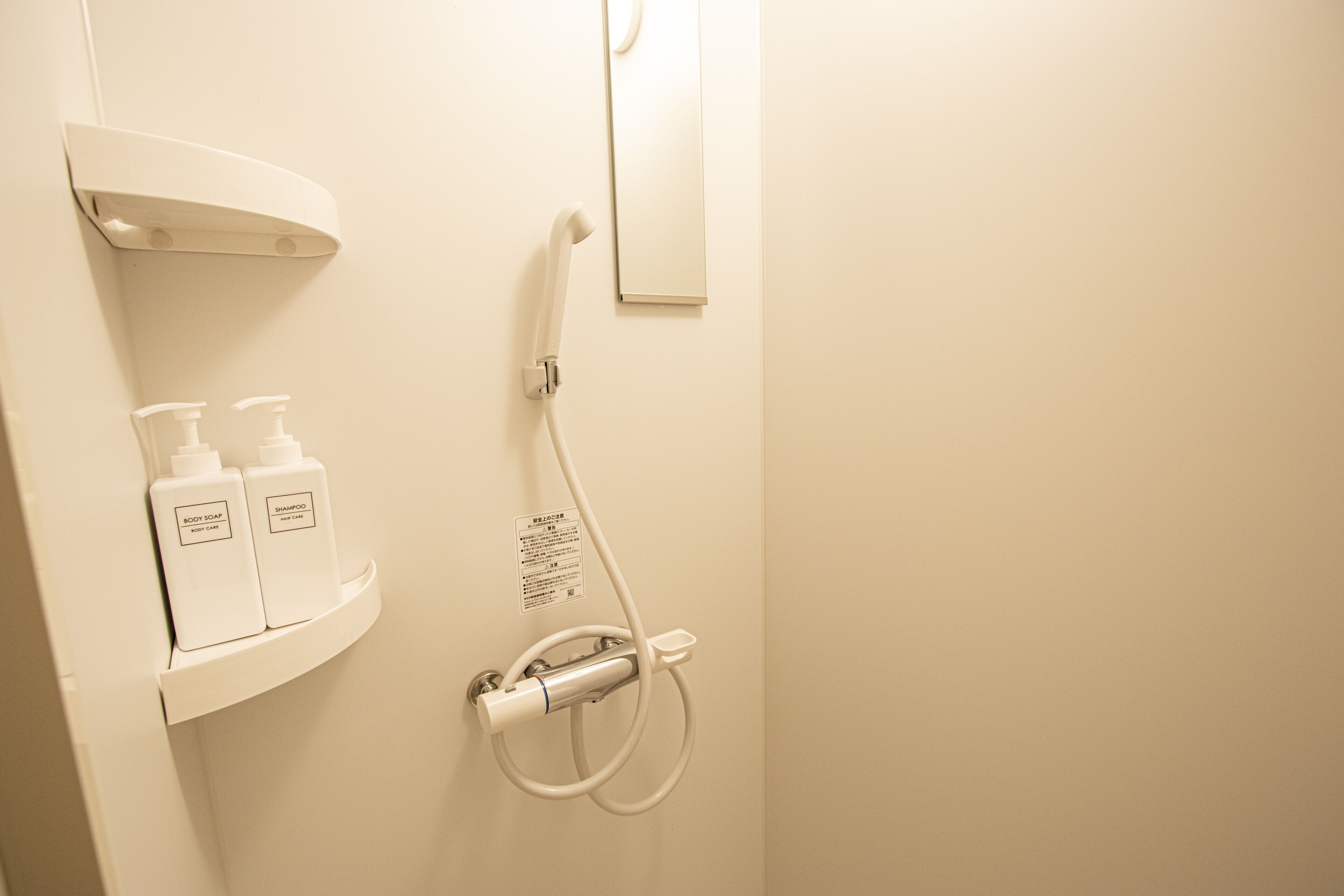 A bathroom with a shower, a shelf with two bottles of shampoo and body wash, and a mirror.