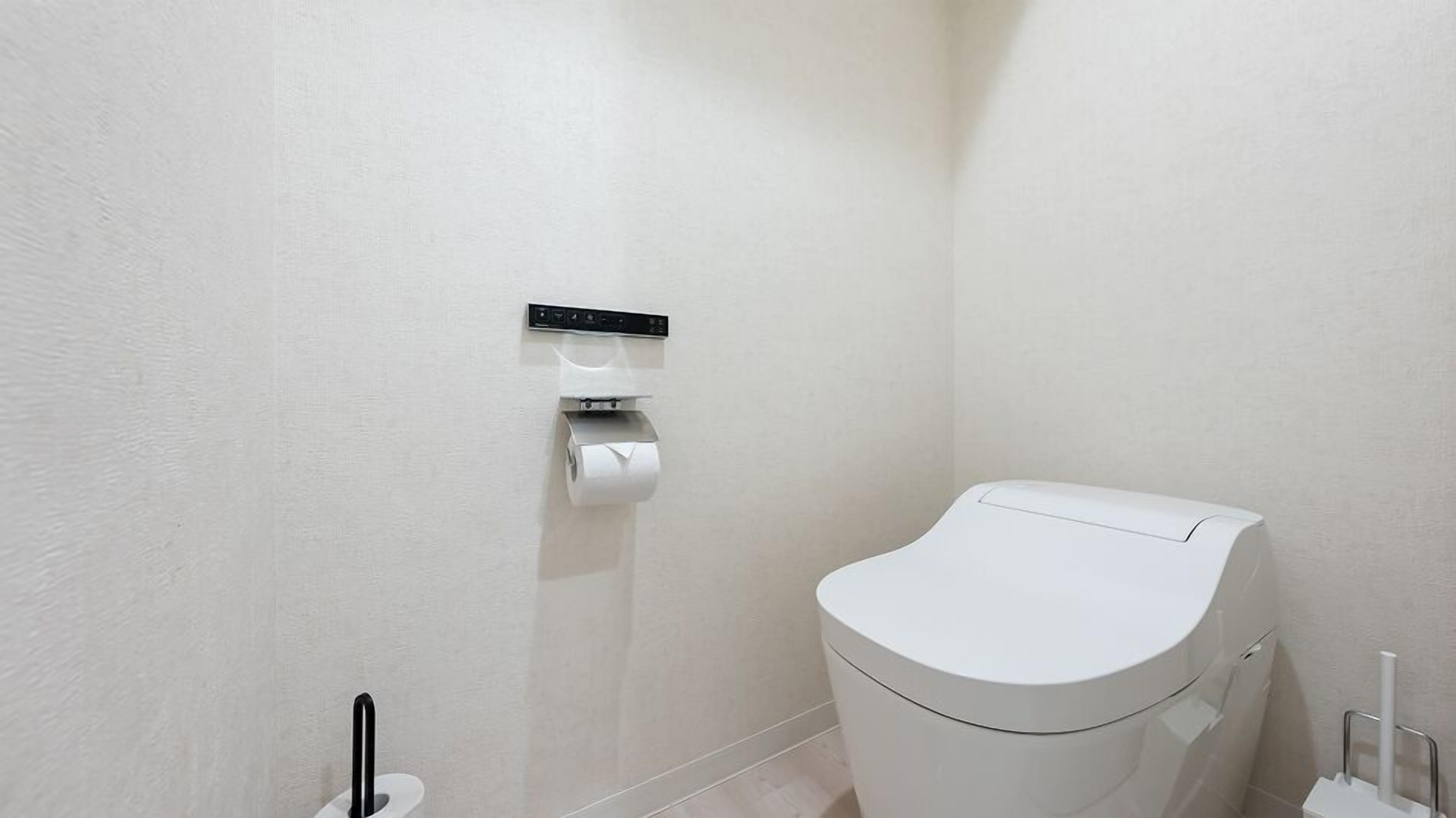 A modern bathroom with a toilet, a hand dryer, and a paper towel dispenser mounted on the wall.