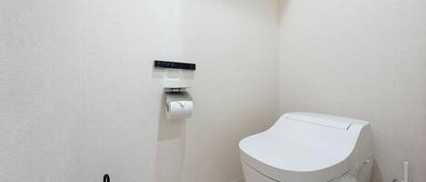A modern bathroom with a toilet, a hand dryer, and a paper towel dispenser mounted on the wall.