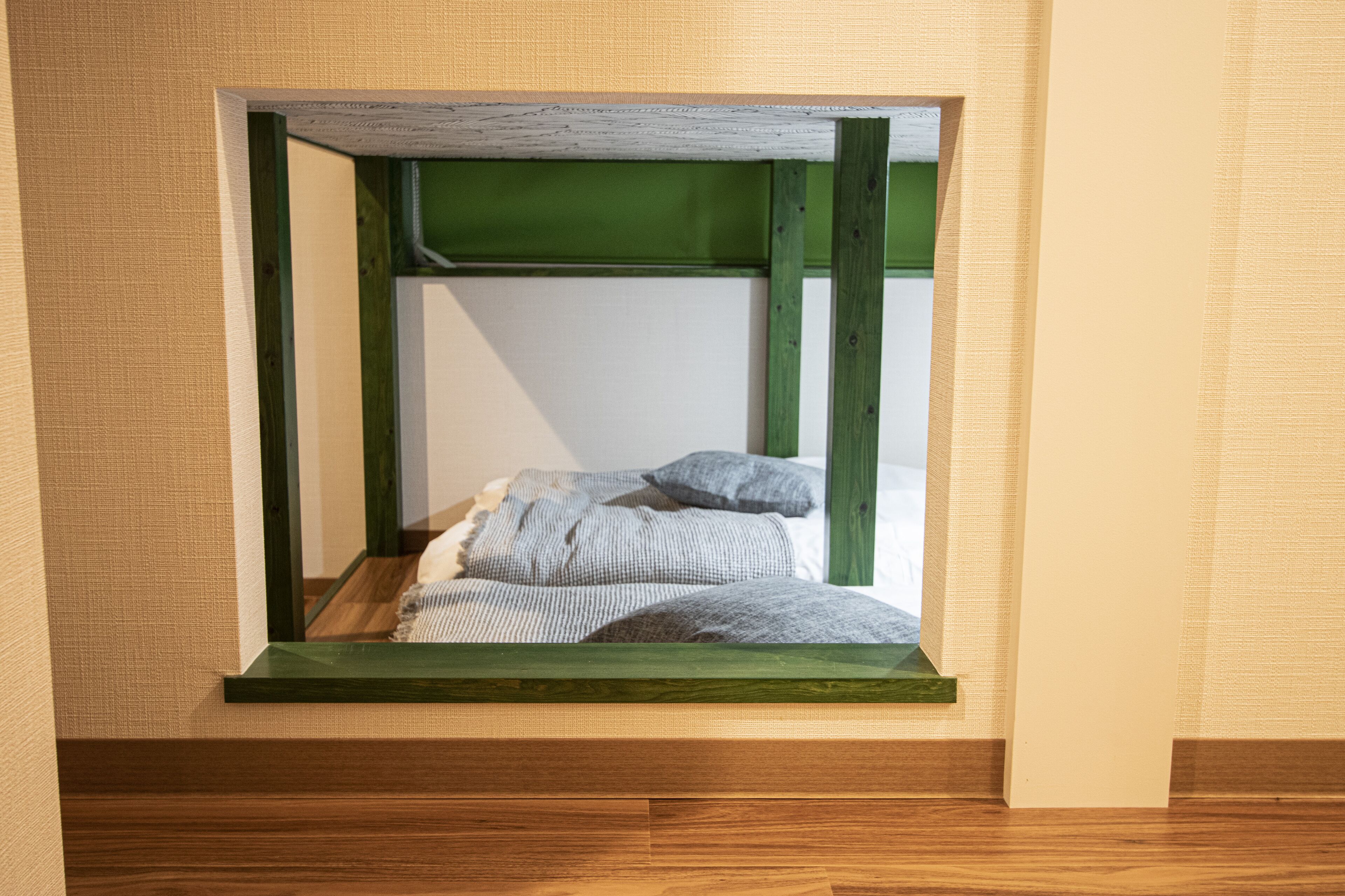 A small, enclosed sleeping area with a wooden frame and a green headboard, featuring a bed with striped bedding and two pillows.