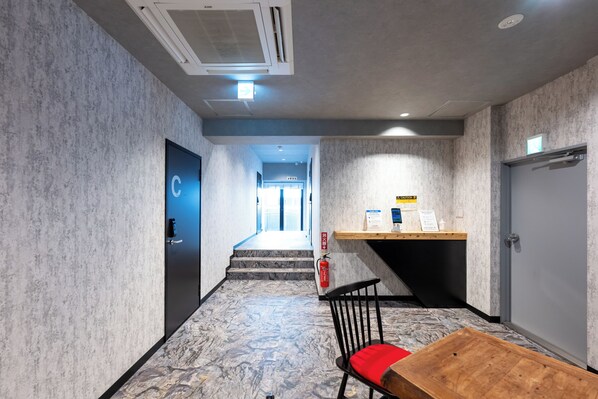 A hotel lobby with a marble floor, a wooden table, a black chair with a red cushion, a reception desk, and a staircase leading to the upper floor. - GRAND CAVE MOTOMACHI (Yokohama)