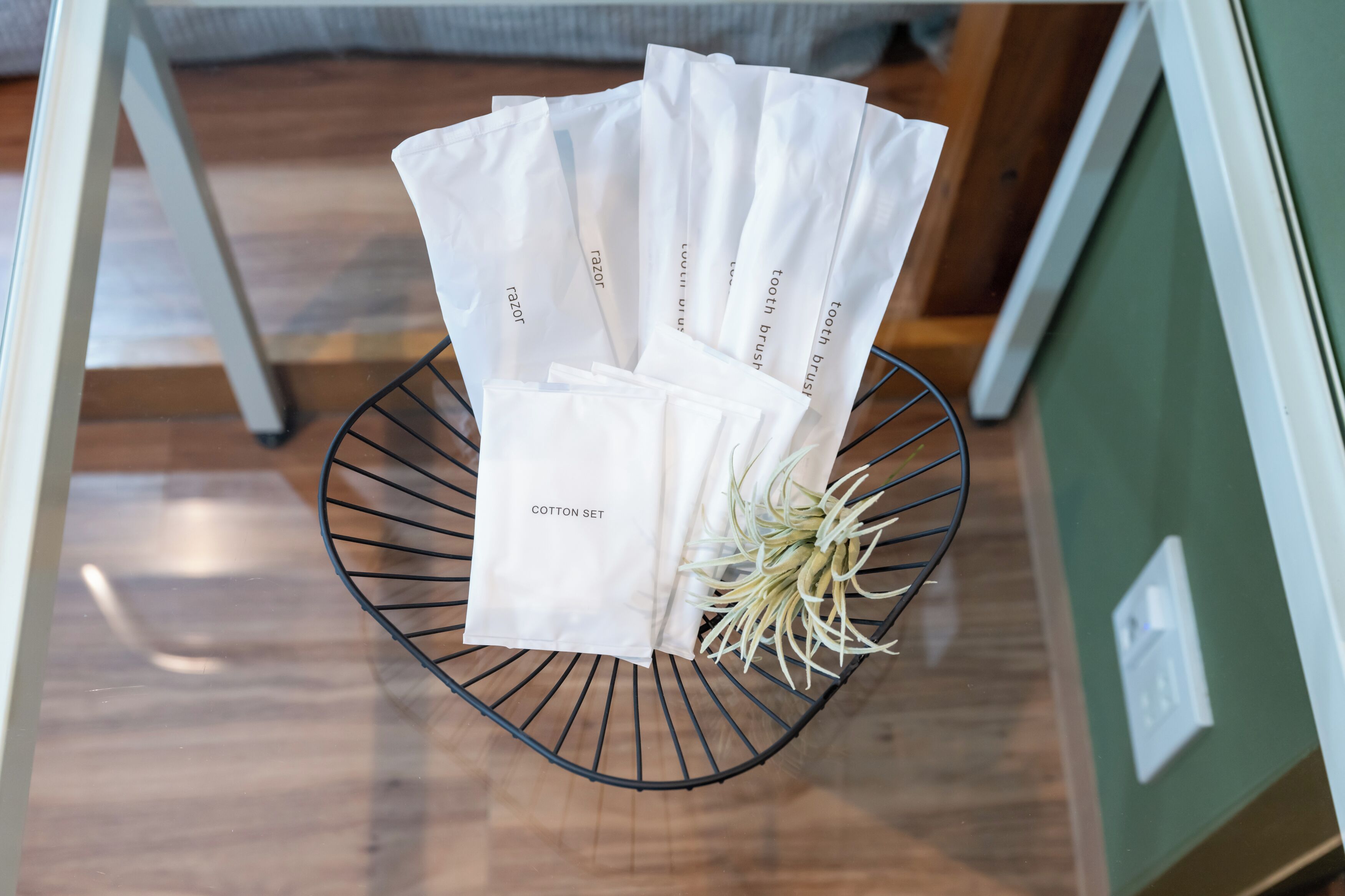 A metal wire basket containing several white bags labeled "razor" and "cotton set" on a wooden floor.