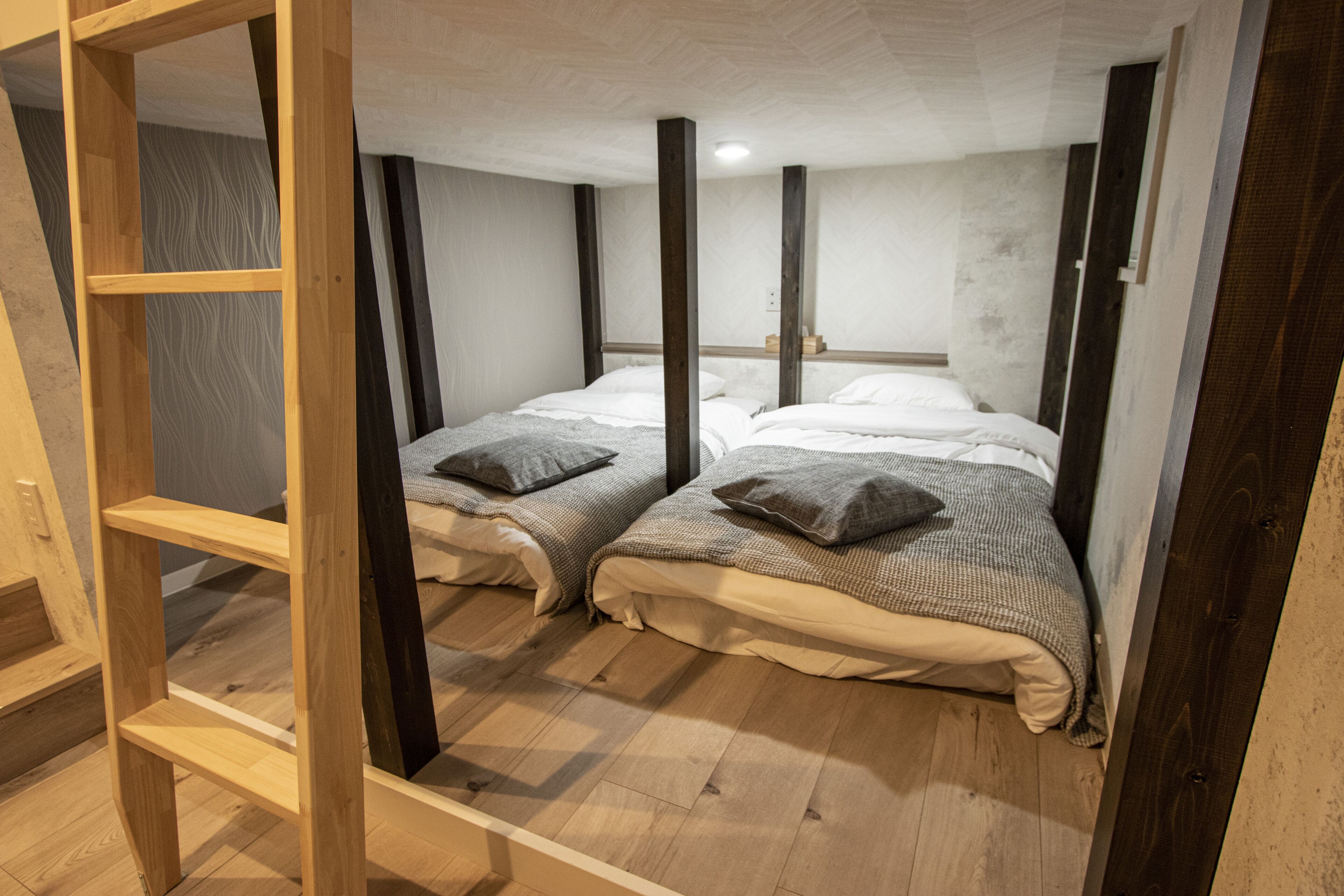Quarto com duas camas, vigas de madeira, um prateleira e teto branco.