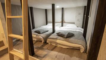Quarto com duas camas, vigas de madeira, um prateleira e teto branco.
