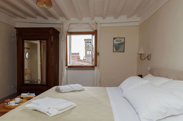 Habitación de hotel con cama, armario de madera, ventana con vistas a una torre y lámpara de pared.