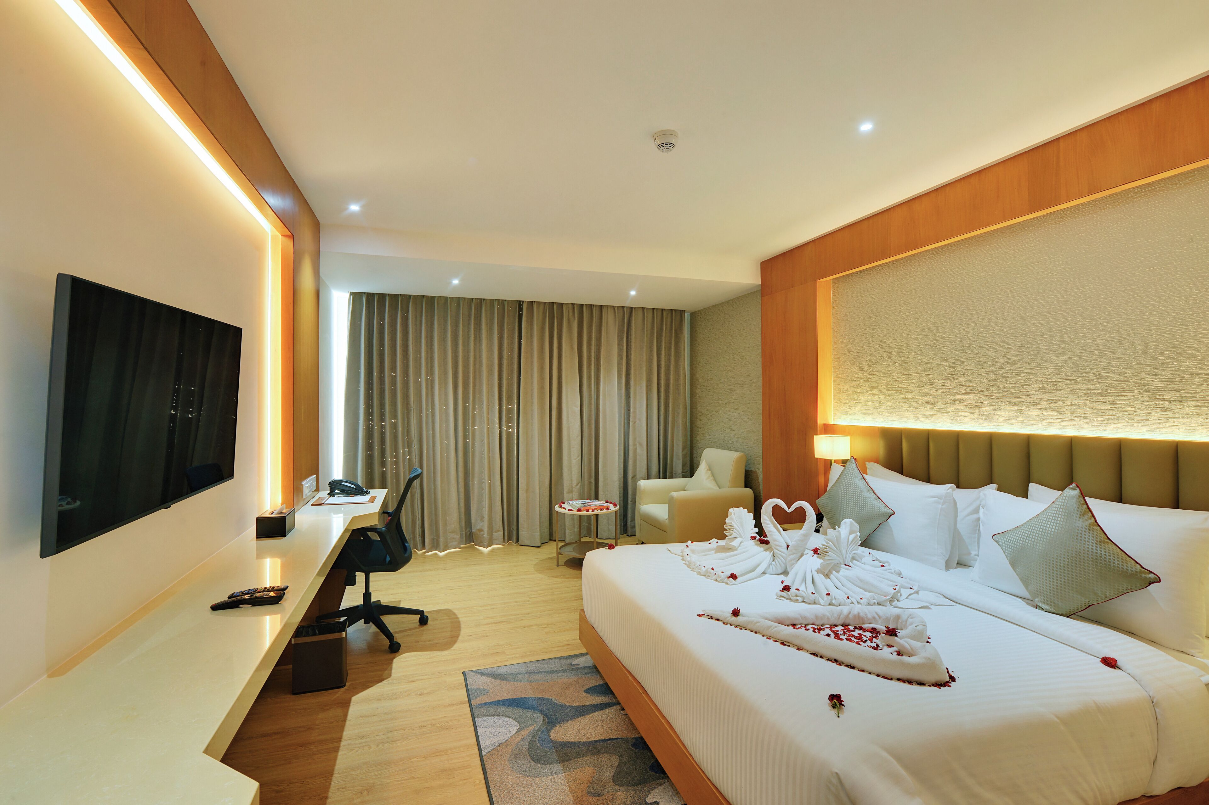 A hotel room with a bed, a desk, a chair, a TV, and a window with curtains.