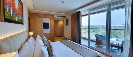 A hotel room with a large bed, a flat-screen TV, a balcony with a table and chairs, and a scenic view.