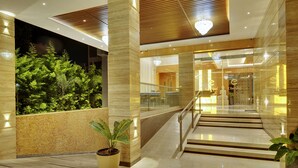 Um hall de hotel moderno com entrada de vidro, escada e uma grande planta em vaso.
