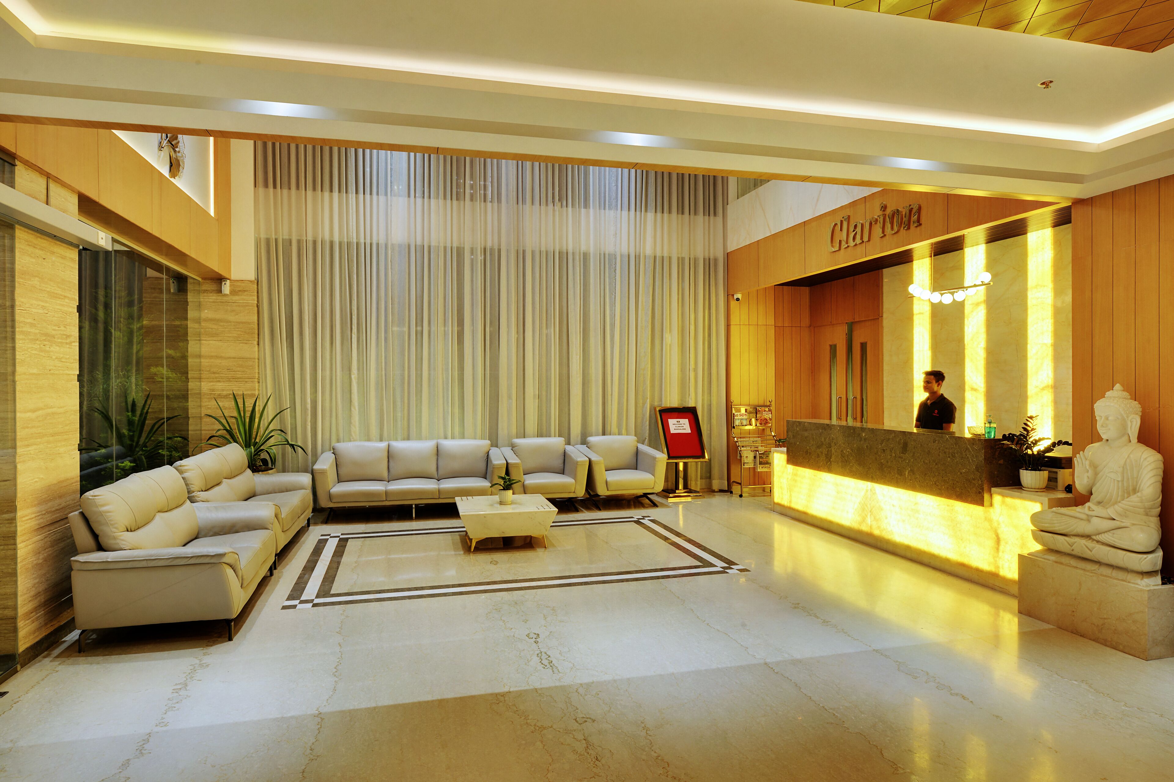 A modern lobby with a reception desk, a Buddha statue, and a seating area with sofas and a coffee table.