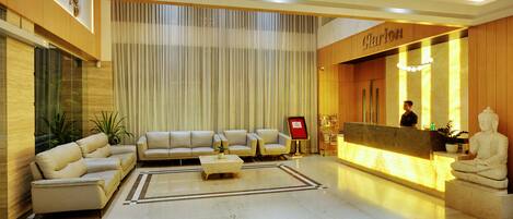 A modern lobby with a reception desk, a Buddha statue, and a seating area with sofas and a coffee table.