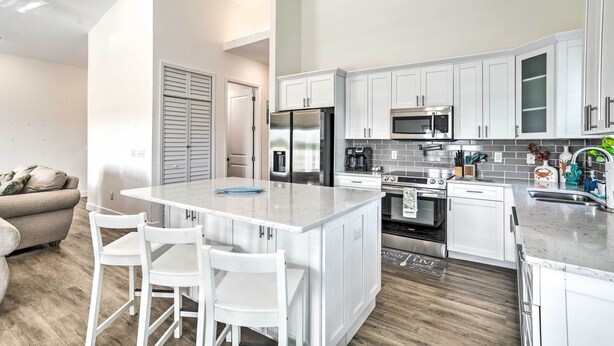 A modern kitchen with white cabinetry, stainless steel appliances, and a central island with bar stools. - Tampa House w/ Patio, Near Downtown & Beaches! (Tampa)