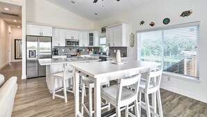 A modern kitchen with white cabinetry, a central island with bar stools, a stainless steel refrigerator, and a ceiling fan. - Tampa House w/ Patio, Near Downtown & Beaches! (Tampa)