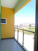 A balcony with a yellow wall, a metal railing, and a view of a street with vehicles and buildings.