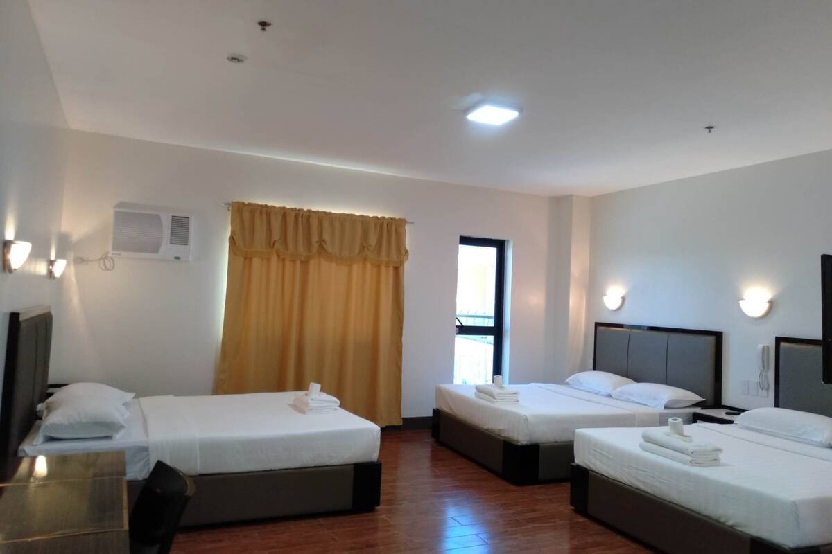 Een hotelkamer met twee enkele bedden, een kleine tafel, een stoel, een raam met gordijnen en een wandairconditioner.